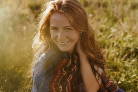 gently and sheepishly smiling girl with natural beauty in ethno cape against the background of...