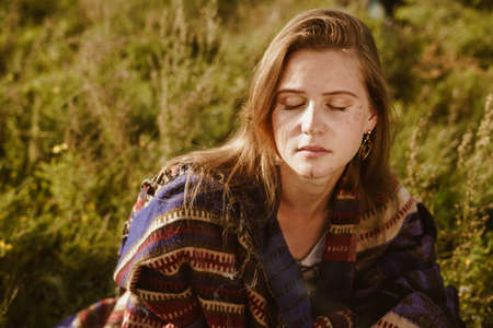 looks down with attentive gaze with sadness on the face of a girl in an ethno cape sitting in the...
