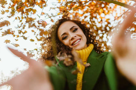 girl with a joyful smile in bright clothes pulls her hands forward against the background of autumn leaves. High quality photoの写真素材