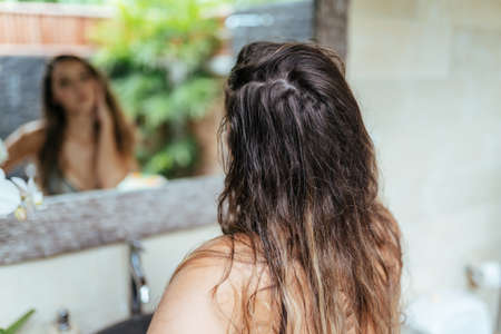 Girl with wet hair looks in the mirror in the bathroom. High quality photoの写真素材