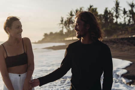 A man with a smile takes a woman smiling at him in response against a backdrop of ocean of palms and...