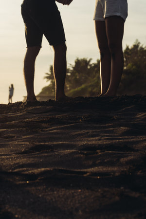on the black sand against the background of palm trees visible in the distance standing a man and a woman whose legs are visible in the photo. High quality photoの写真素材
