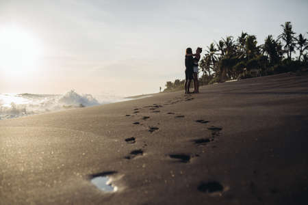 on the black coastal sand in the distance amid palm trees hugged by a loving couple. High quality photoの写真素材