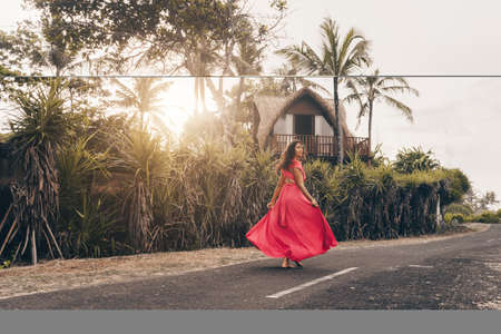 In Bali on the tarmac past the villa and palm trees in a long bright dress goes looking over the shoulder of the brunette. High quality photoの写真素材