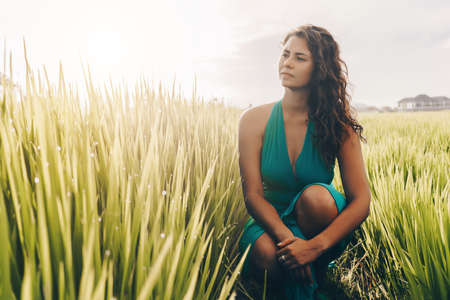 Dark-haired beauty crouched among the thickets of rice posing and looking into the distance. High quality photoの写真素材
