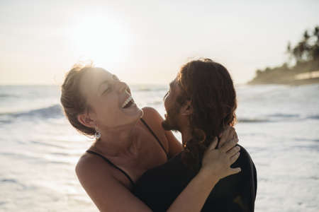 Amid the ocean waves, a man hugs a woman and they laugh cheerfully. High quality photoの写真素材