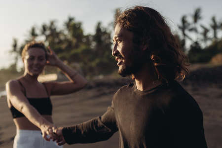 The man in the foreground holds the womans hand and pulls her against her against the palm trees....