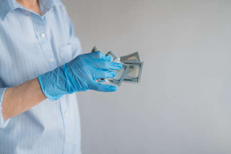 A hand in a blue latex glove counts money on a white background. Dressed in a shirt. High quality photoの写真素材