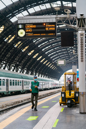 4.10.2021 Milan, Italy - Milano Centrale railway station. A male station worker walks along an empty platform wearing a medical mask on his face.のeditorial素材