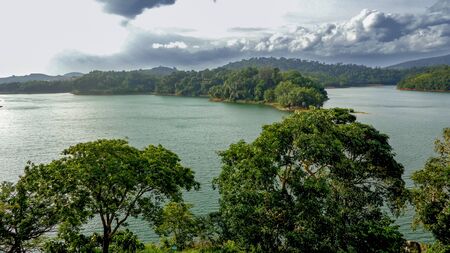 Landscape view of a lake surrounded by forested hills with cloudy skiesの写真素材