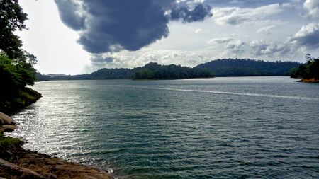 Landscape view of a lake surrounded by forested hills with cloudy skyの写真素材