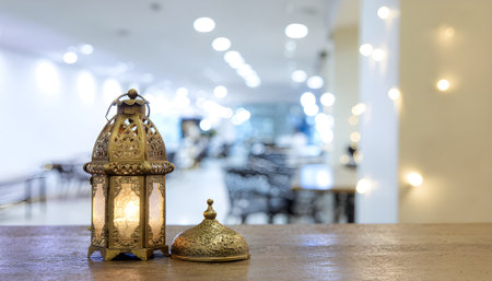 Golden Ramadan Lantern on Wooden Table with Blurred Restaurant Backgroundの素材