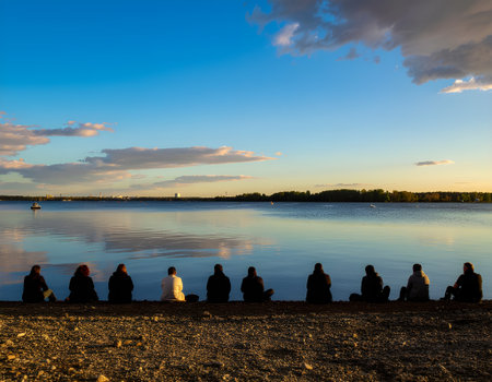 Group of People Silhouetted by a Lake at Sunset, Representing Peace and Reflectionの素材