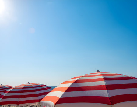Classic red and white striped beach umbrellas under a brilliant sunny blue sky, a perfect scene for a summer vacation getaway.の素材