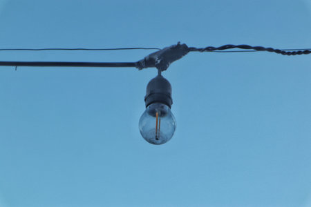 A minimalist industrial-style hanging lamp featuring a bare bulb and exposed black braided cable, against a clean, light background.の写真素材