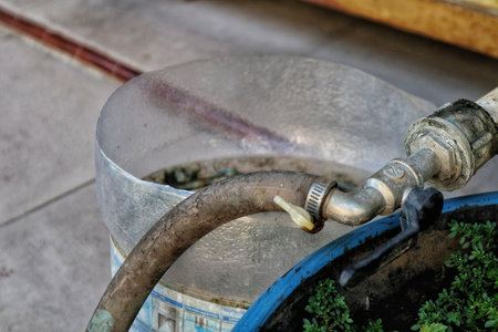 A simple home water tap connected to a faucet, with a repurposed large water gallon serving as a makeshift bucket (becket) for collecting water, showcasing everyday utility.の写真素材