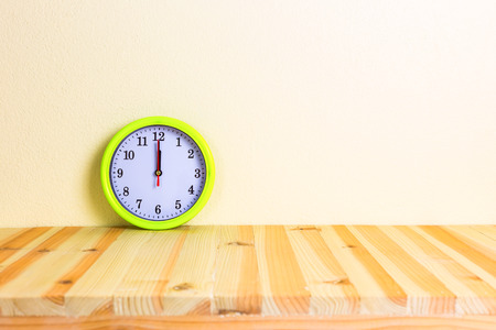 Clock on wood table with concrete wall background.
