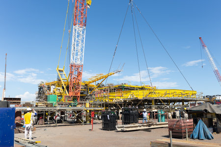 Heavy lifting with crane hoisting massive oil rig platform under clear blue sky. Showcases precision engineering and construction in natural gas, oil.の写真素材