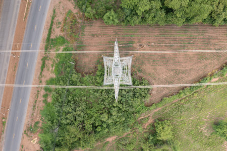 Aerial view of power line and tall electrical transmission tower standing amidst natural landscape...