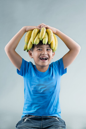 asian child holding banana on head and grey backgroundの写真素材