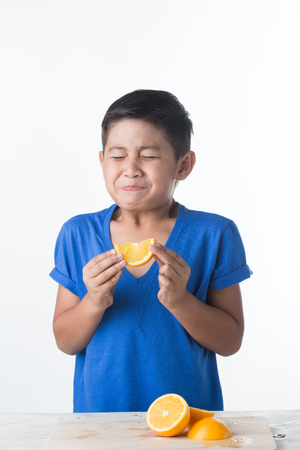 Asian child with a pout biting sour lemon. Sour taste.の写真素材