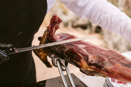 Iberian ham cutter. Traditional spanish jamon serrano pata negra with selective focus. Professional cutter cutting delicious Iberian ham.の写真素材