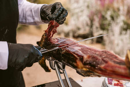 Iberian ham cutter. Traditional spanish jamon serrano pata negra with selective focus. Professional cutter cutting delicious Iberian ham.の写真素材