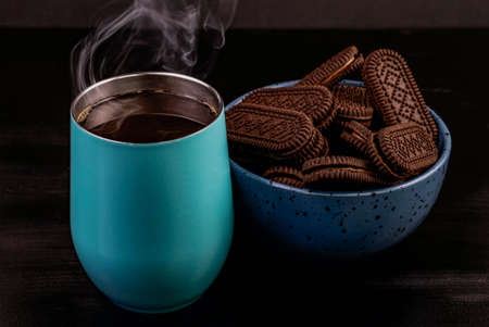 Light blue coffee mug freshly served, with a bowl of chocolate chip cookies on the sideの写真素材