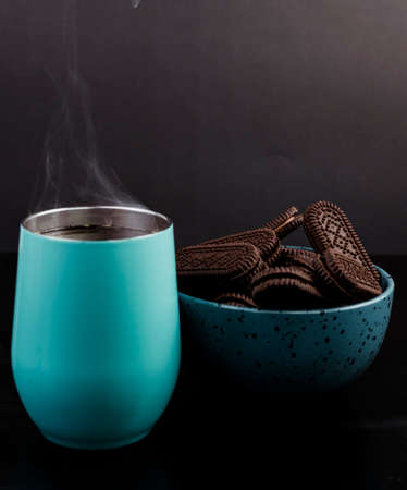 Light blue coffee mug freshly served, with a bowl of chocolate chip cookies on the sideの写真素材