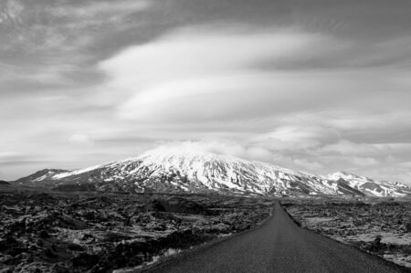 Snowy mountains, volcanic land, meadow, amazing clouds and a lonely path in black and white