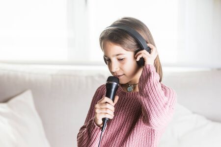 Girl singing happily with earphones and mic in home interiorの写真素材