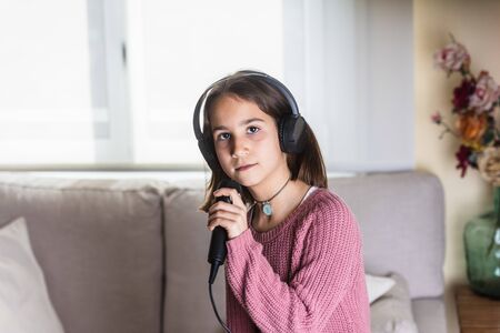 Girl singing happily with earphones and mic in home interiorの写真素材