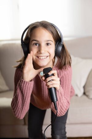 Girl singing happily with earphones and mic in home interiorの写真素材
