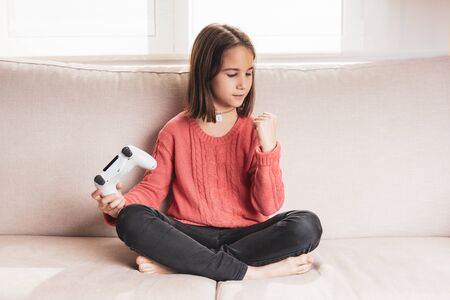 Little girl playing at home with game console sitting on the sofa