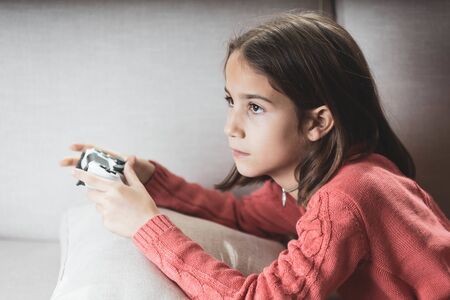 Little girl playing at home with game console lying on the sofaの写真素材