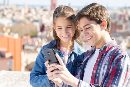 Two smiling siblings looking at the mobile on the rooftop