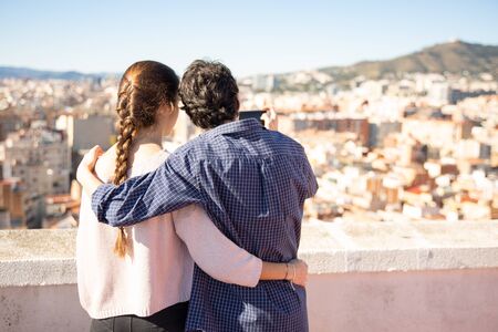 Embracing wedding couple making photographs of the urban landscape from the rooftopの写真素材