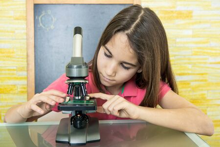 Little girl at home alone observing and studying under a microscope