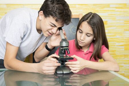 Sister and brother at home observing through a microscopeの写真素材