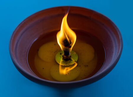 Large anti-mosquito candle burning in a ceramic clay pot on a turquoise blue backgroundの写真素材