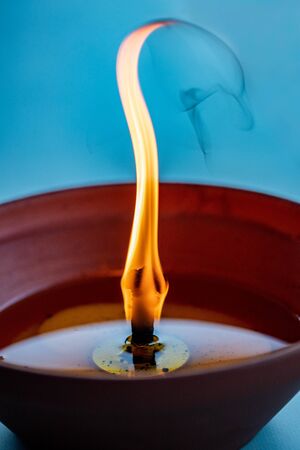 Wavering wick of an anti-mosquito candle burning in a ceramic clay pot on a turquoise blue...