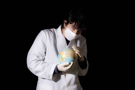 Young doctor with face mask stroking a world globe on black backgroundの写真素材