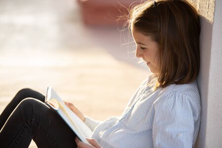 Smiling girl reading a book sitting on the rooftopの写真素材