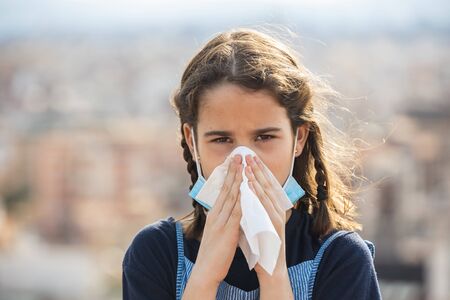 Sick little girl with allergy covering her mouth with a handkerchief in the city with pollutionの写真素材