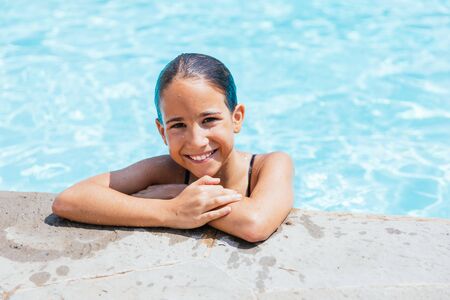 Girl looking at the camera leaning on the edge of the poolの写真素材