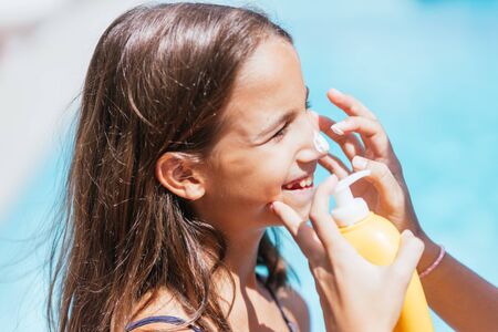 Woman's hands applying sun protection to a girl on summer vacation in the poolの写真素材