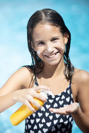 Little girl looking at the camera while applying suntan lotion on her handの写真素材