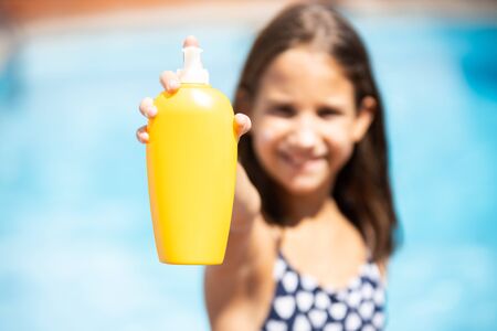 Happy girl in the pool showing a bottle of sunscreen with dispenserの写真素材
