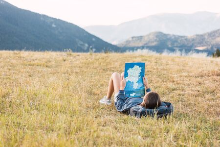 Female traveler consulting map lying on the grass among mountains