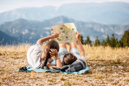 young travelers lying on the grass looking at a map in a beautiful place with the mountains in the...